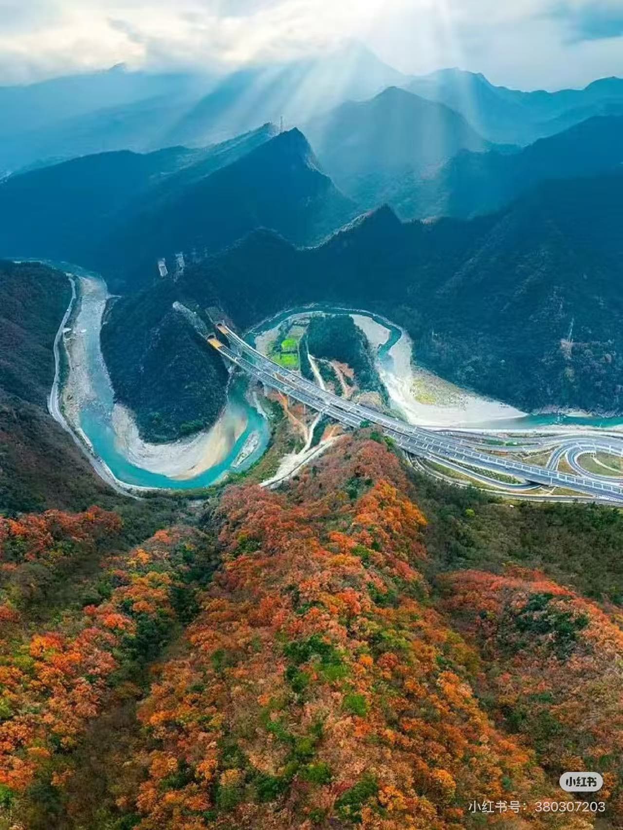 Breathtaking aerial view of autumn mountains, winding river, and a massive highway interchange with sunrays. - ChinaTripTop.